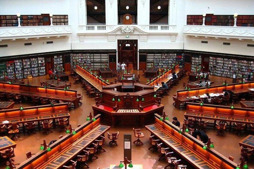 A large, ornate library interior with multiple levels of bookshelves, wooden tables, and reading areas. 1