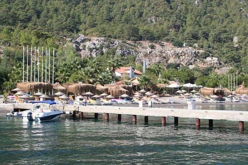 A coastal scene with a pier extending into calm waters, a small boat docked at the pier, and a beach area with umbrellas and thatched-roof structures. 5