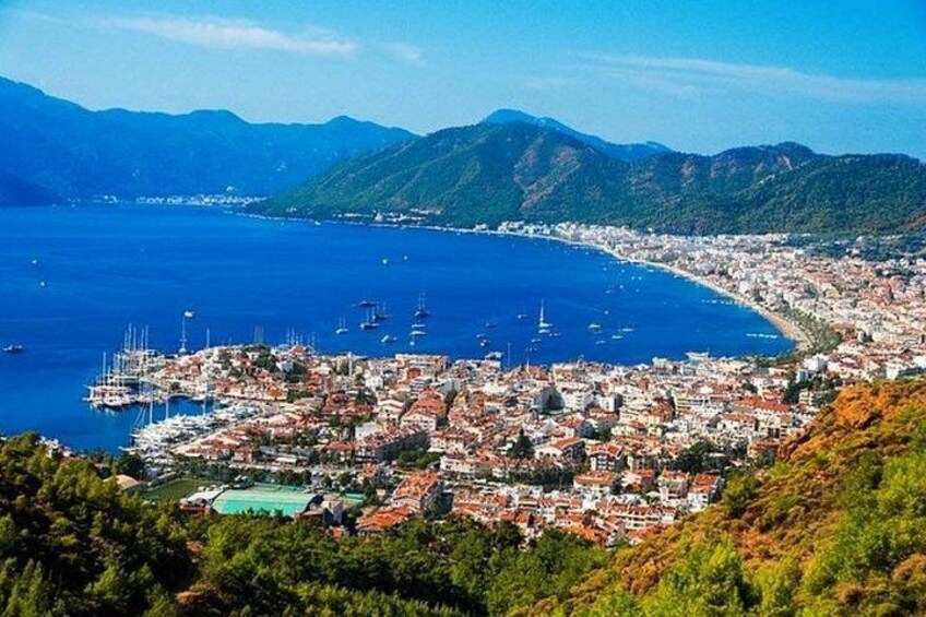 A coastal city with a marina, mountains in the background, and a clear blue sea. 3