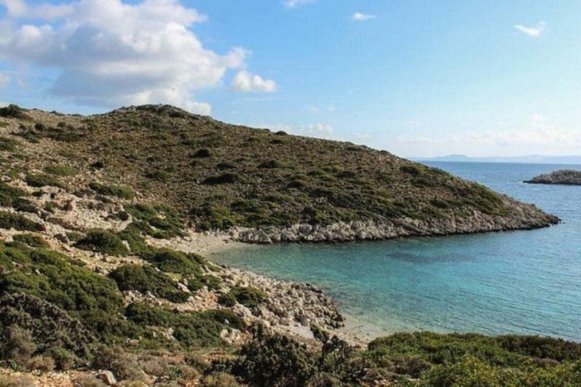 A coastal landscape with a rocky shoreline, clear blue waters, and a hilly terrain. 4