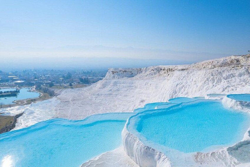 Terraced pools of clear blue water, a white cliff, and a distant cityscape. 4