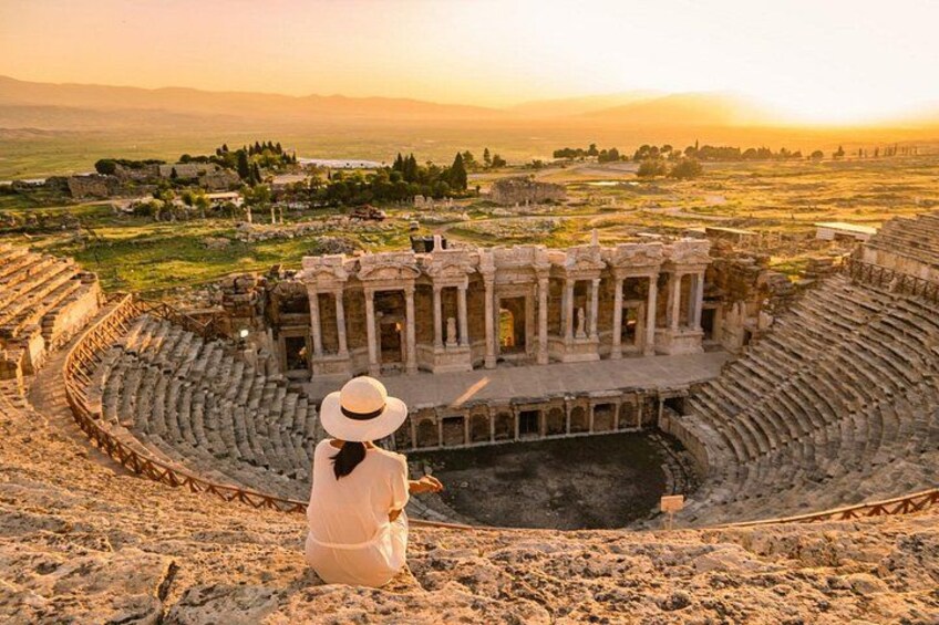 An ancient amphitheater with ruins, a person in a white dress and hat, and a sunset in the background. 3