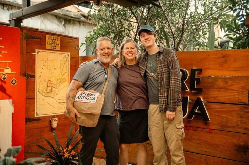 Three people standing in front of a wooden sign with the word 'REJA' and a map. 2