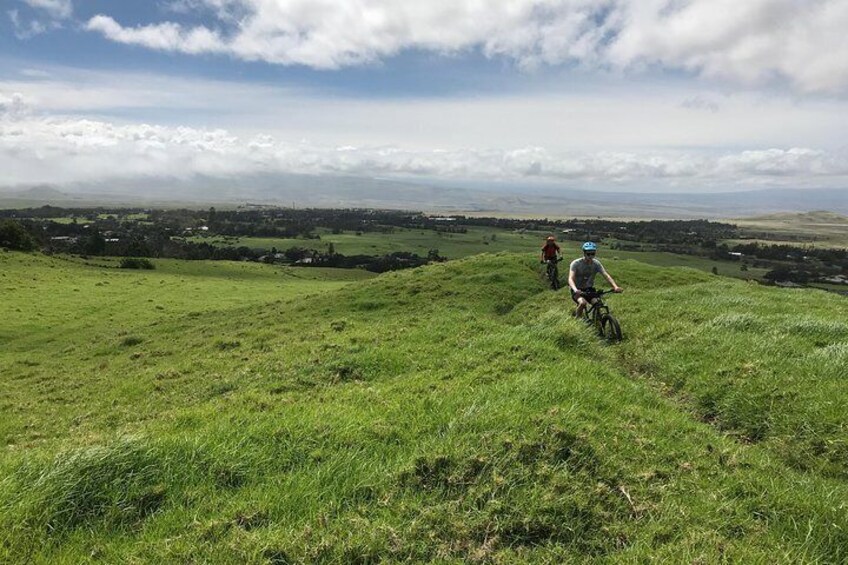 Two cyclists on a grassy hill with a distant landscape. 5