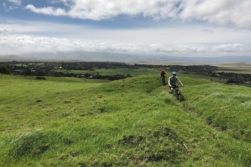 Dos ciclistas en una colina cubierta de hierba con un paisaje lejano. 4