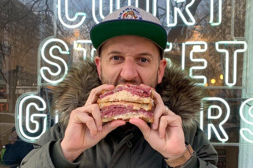 Una persona sostiene un sándwich frente a un letrero de neón que dice 'COURT STREET GROSSES'. 2
