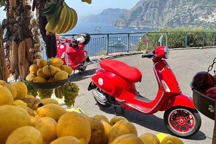 A red scooter parked near a coastal area with a view of the sea and mountains. 1