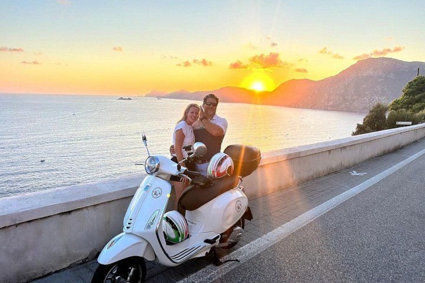 A sunset over a body of water with a scooter parked on the side of a road. 3