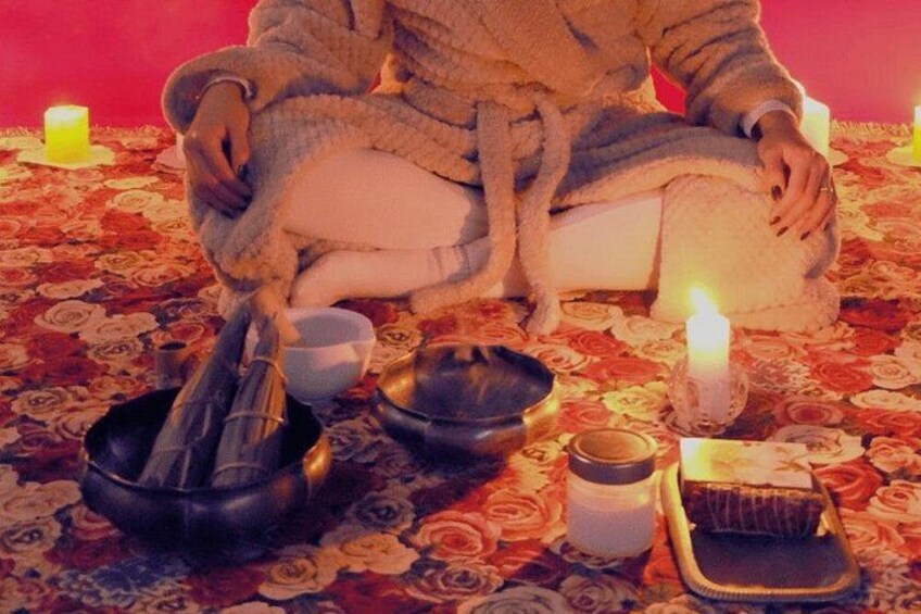 A person sitting on a chair with candles and bowls on a patterned carpet. 4