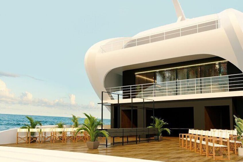A modern cruise ship deck with a white building, outdoor seating, and palm trees. 1