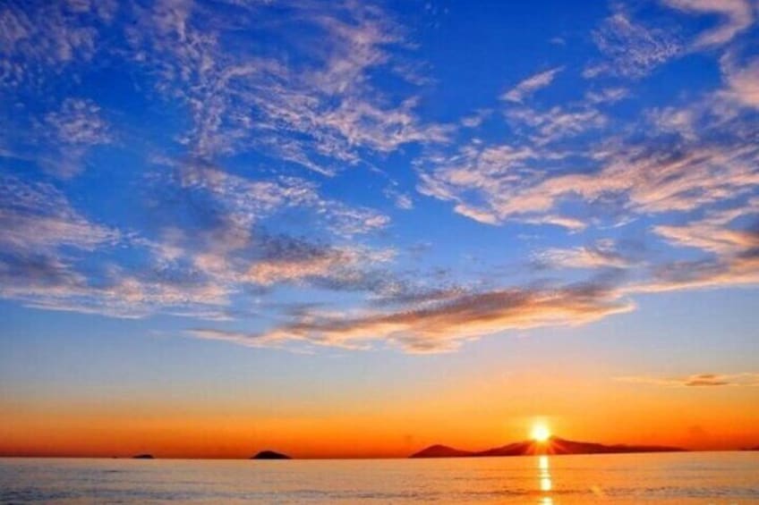 A sunset over a calm sea with a clear sky and distant land. 4