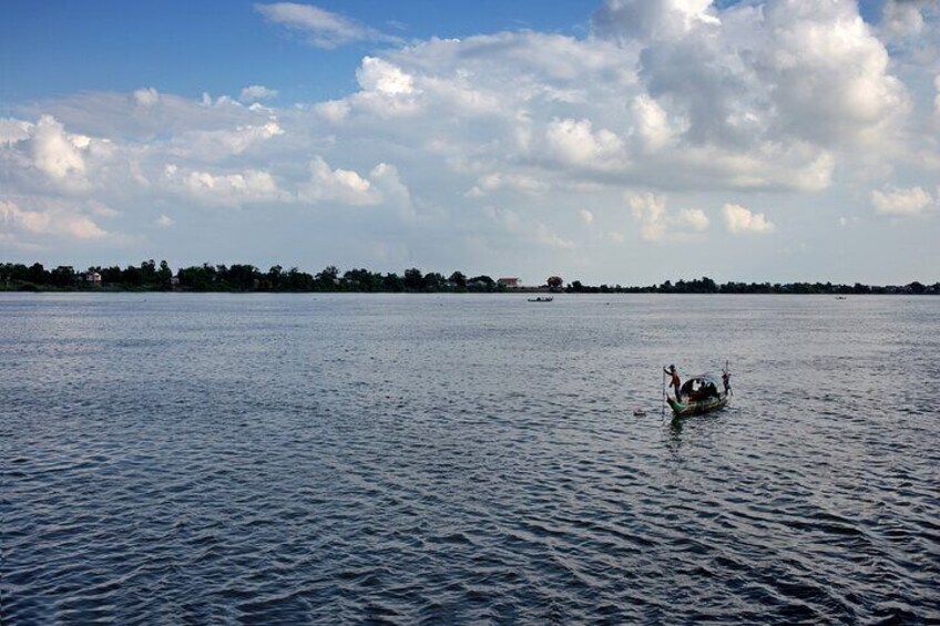 Un lago tranquillo con una piccola barca al centro e una riva lontana con alberi e edifici. 3