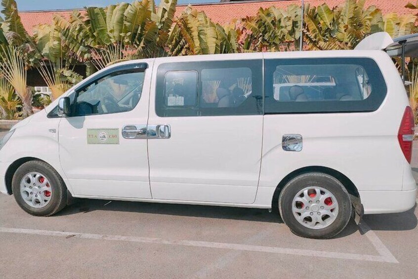 Un furgone bianco parcheggiato su una strada, con un edificio e piante rigogliose sullo sfondo. 4