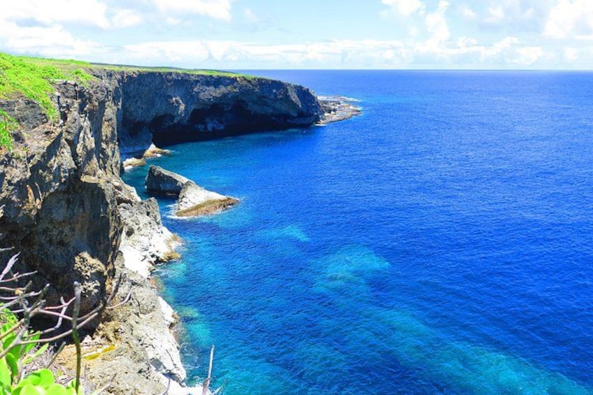 A coastal cliff with clear blue water, rocky terrain, and sparse vegetation. 2