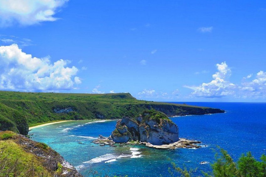 A coastal landscape with a prominent rock formation surrounded by clear blue waters and lush green hills. 3