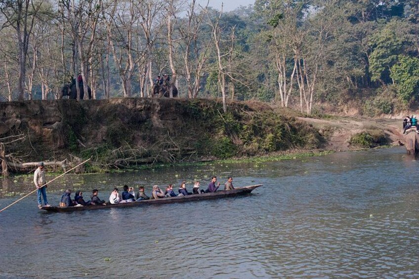 A group of people in a longboat on a river, surrounded by trees and a rocky bank. 1