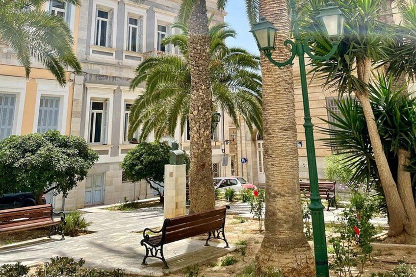A park with palm trees, benches, and a building in the background. 1