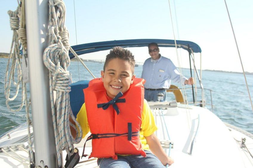 Una persona en un velero con chaleco salvavidas, cuerdas y un cielo despejado al fondo. 5