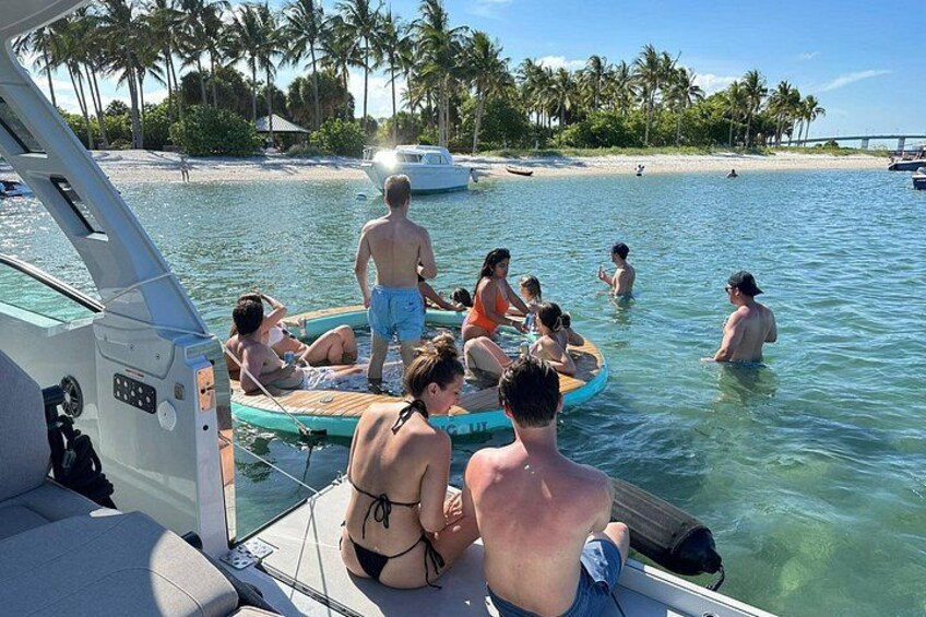 Eine Gruppe von Menschen auf einem Boot, einige im Wasser und andere auf dem Deck, mit einem Strand und Palmen im Hintergrund. 4