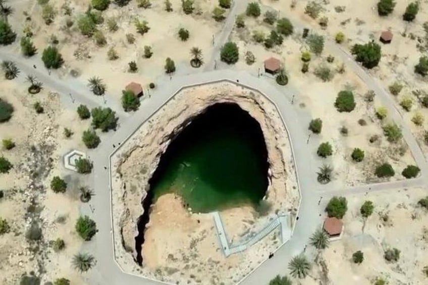 Luchtbeeld van een grote, door mensen aangelegde krater met een groenachtig waterlichaam in het midden, omringd door schaarse begroeiing en enkele gebouwen. 5