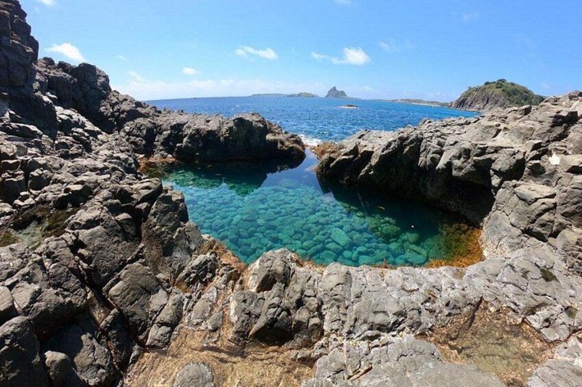 A rocky coastline with clear blue water and a distant island. 1