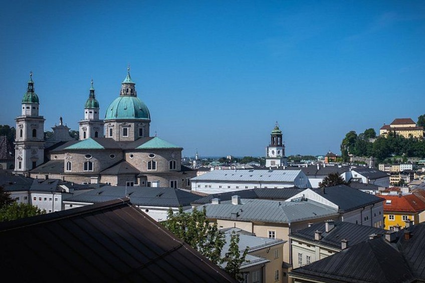 A cityscape with historic buildings, including a prominent church with a green dome and multiple spires, and a clock tower in the background. 5