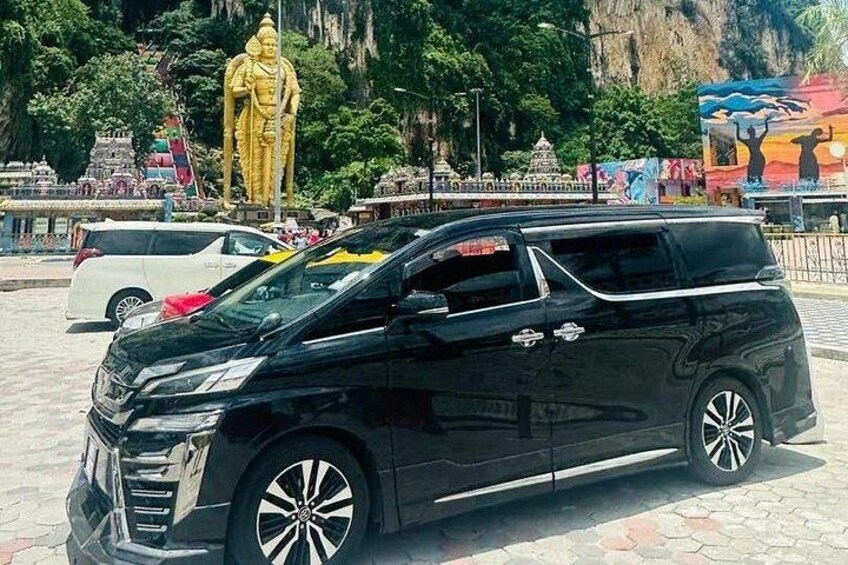 A black minivan parked in front of a large golden statue. 1