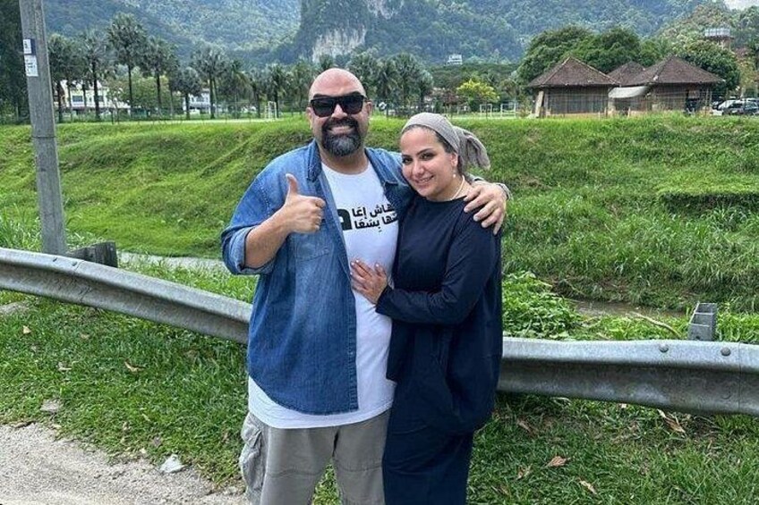 Two people standing by a metal railing with greenery and houses in the background. 3