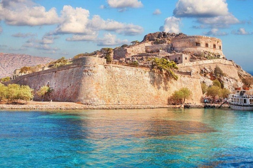 A historic stone fortress by a clear blue sea, with a boat docked nearby. 1