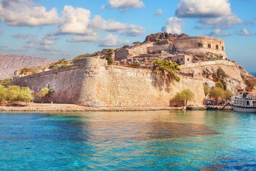 A historic stone fortress by a clear blue sea, with a boat docked nearby. 1