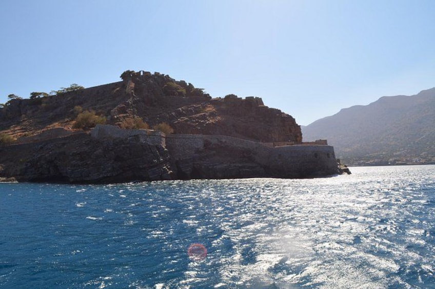 A rocky island with a fortification, surrounded by calm sea and distant mountains. 4
