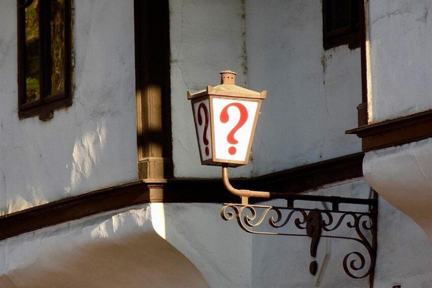 A street lamp with a question mark on it, attached to a building with white walls and dark trim. 4