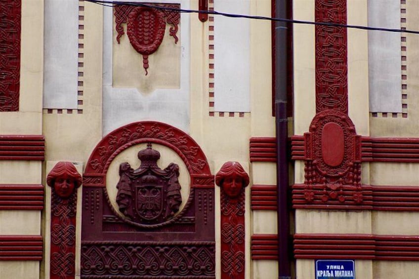 A building facade with intricate red and beige architectural details, including a prominent archway with a crest and a sign reading 'YURILYA KRAJSA-MURINAHA'. 2