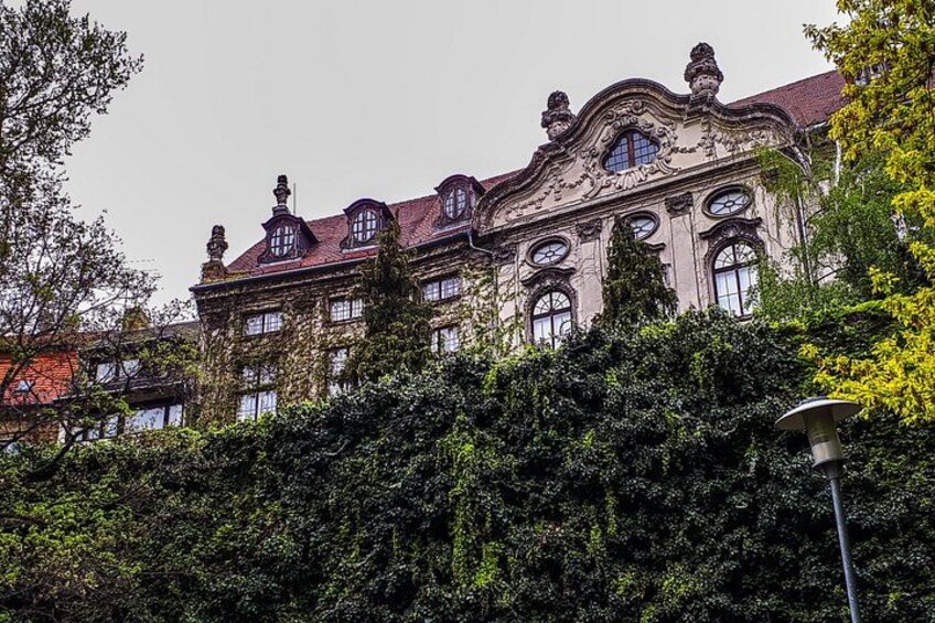 En historisk byggnad med utsmyckad arkitektur, omgiven av frodig grönska. 1