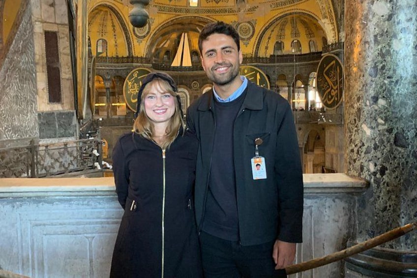 Un homme et une femme se tiennent devant un bâtiment historique, dont l’architecture présente des détails complexes et qui est doté d’un mur en pierre. 2