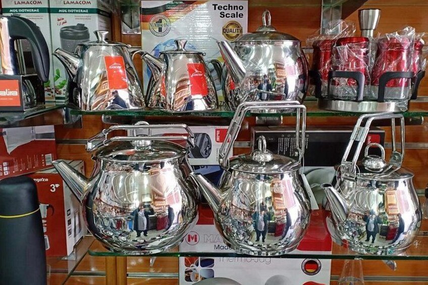 A display of silver teapots with reflective surfaces and a sign indicating a Techno Scale. 2