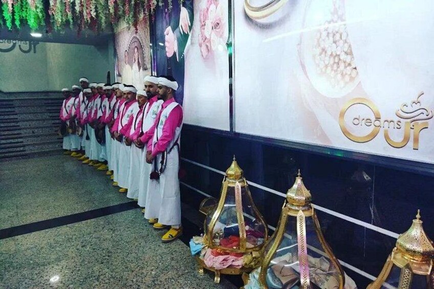 A group of men in traditional attire standing in a line, a staircase, and decorative lamps. 4