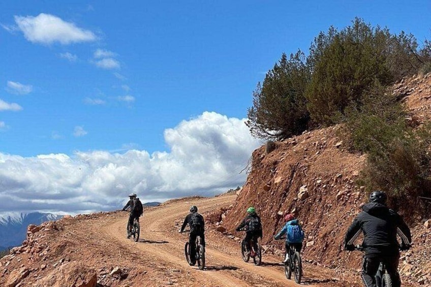 A group of cyclists on a dirt trail with a mountainous backdrop. 1