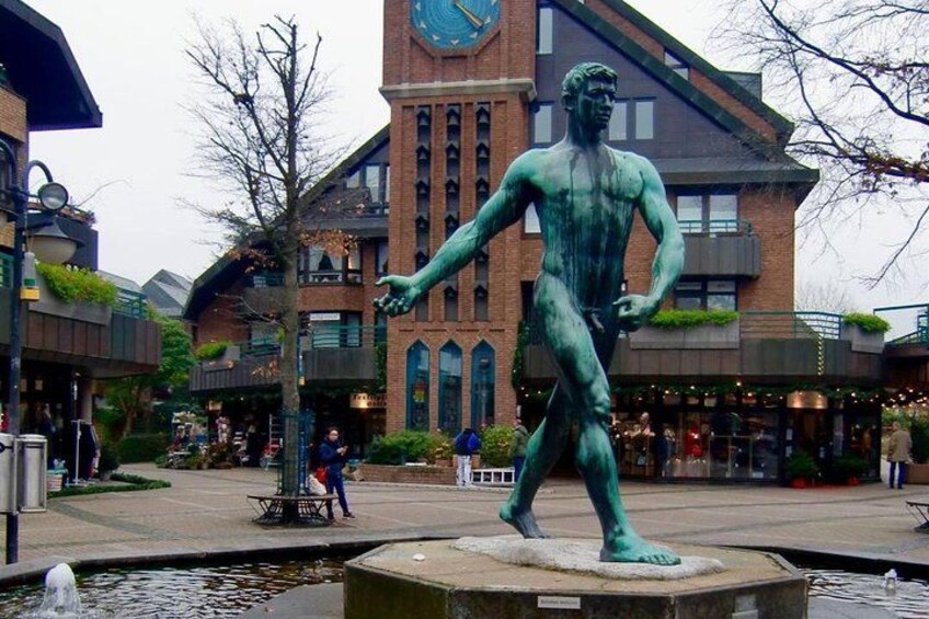 A bronze statue of a muscular man in a public square with a clock tower in the background. 1