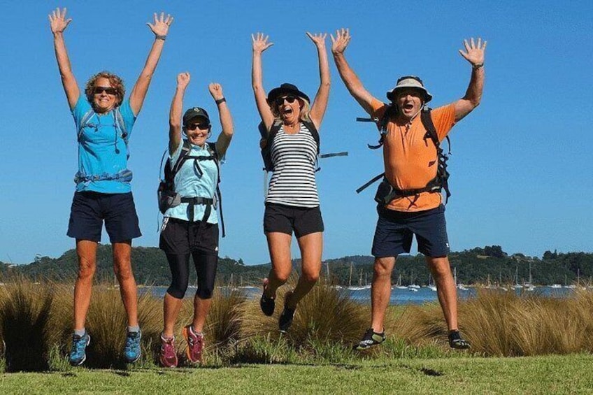 Four people jumping in a grassy field with a clear sky and distant boats on water. 1