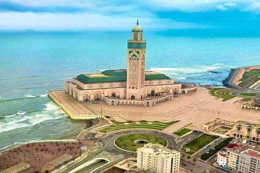 Een grote moskee met een hoge minaret, omgeven door een kustgebied met een weg en gebouwen. 1