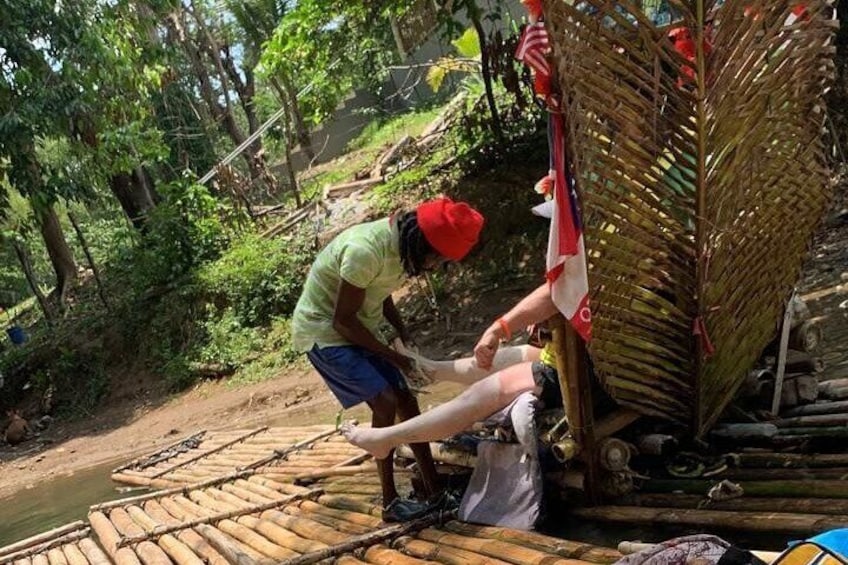 Une personne portant une casquette rouge et un t-shirt vert travaille sur un radeau en bambou dans une rivière bordée de végétation luxuriante. 5