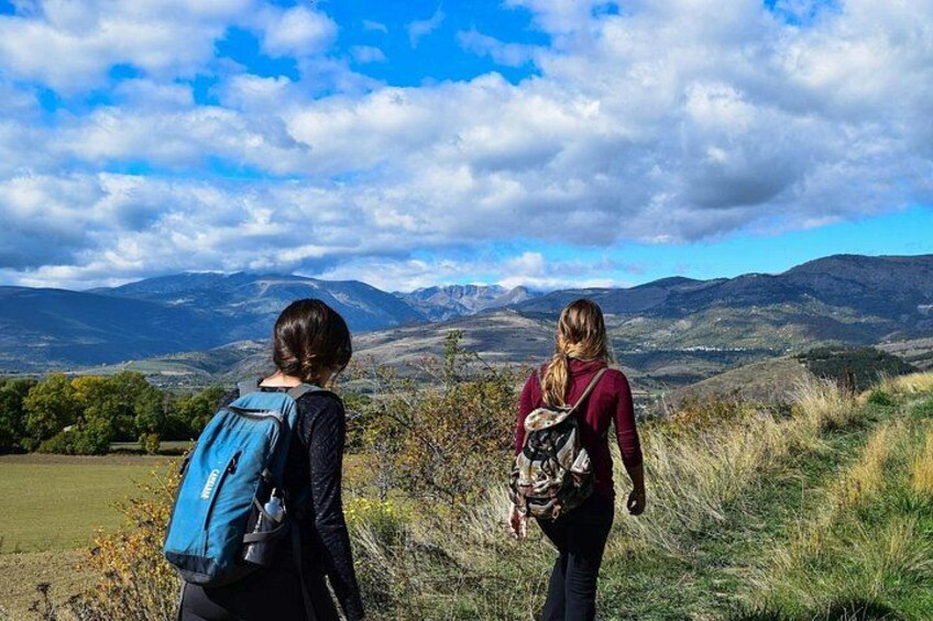 Two people hiking on a grassy hill with a mountainous landscape in the background. 5