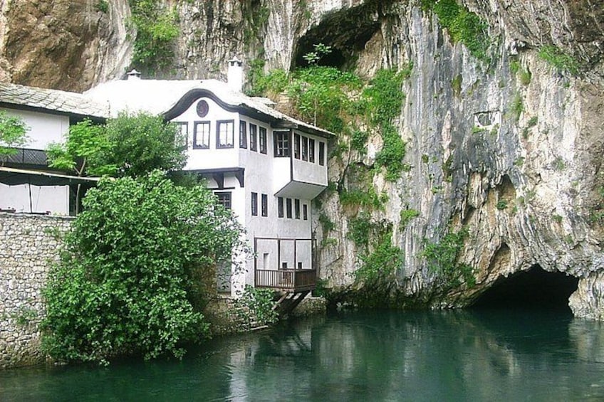 A house with a balcony overlooking a river, set against a rocky cliff. 2
