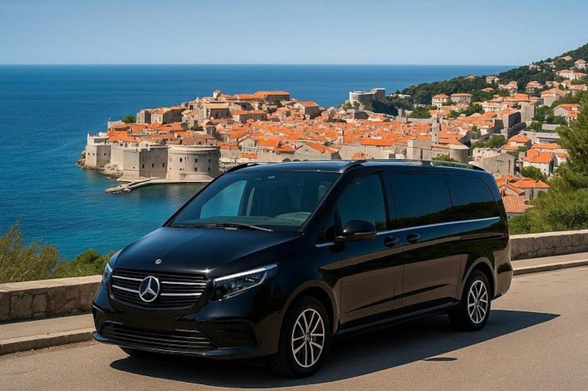 A black Mercedes-Benz minivan parked on a road with a coastal town and sea in the background. 1
