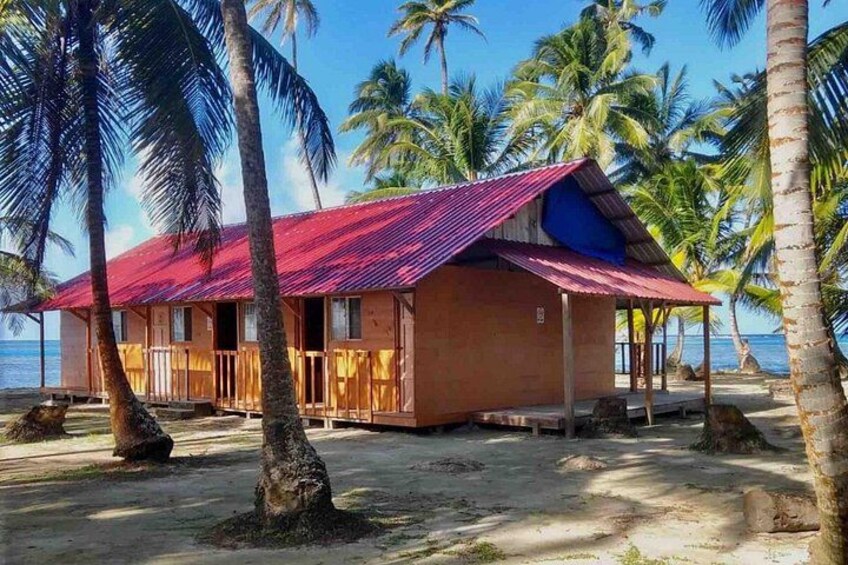 A beach house with a red roof, surrounded by palm trees and the ocean. 4