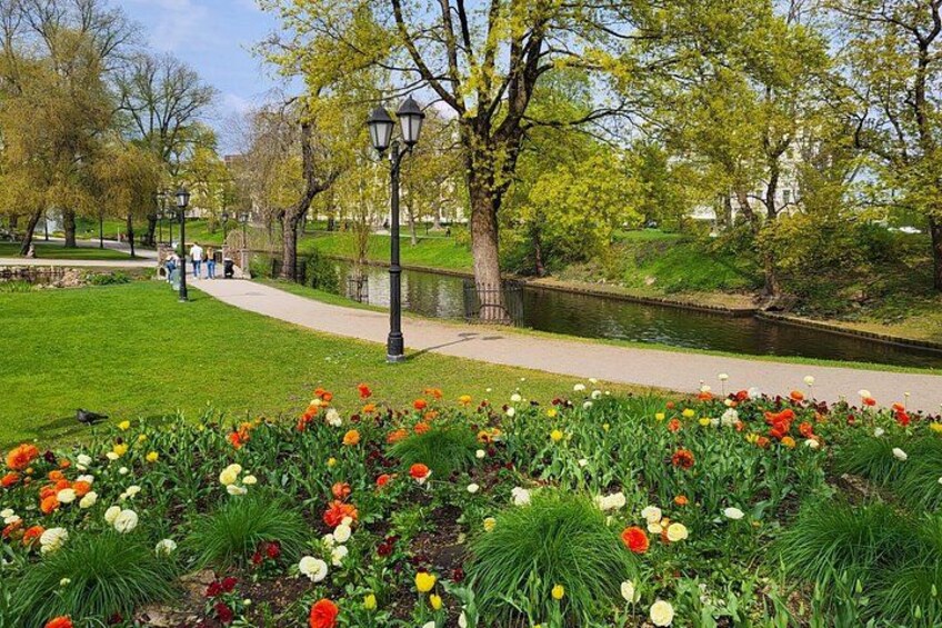 A park with a pathway, trees, a body of water, and colorful flowers. 3