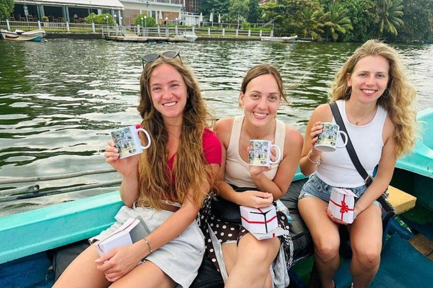 Drie mensen in een boot met mokken, water en een steiger op de achtergrond. 2