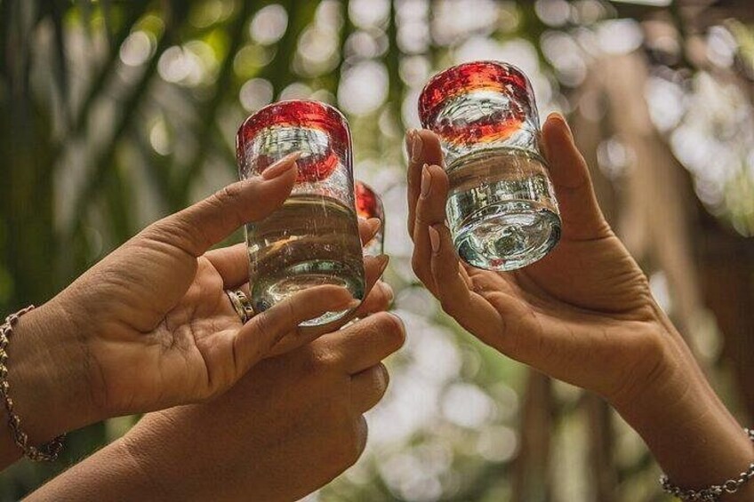 Dos manos sosteniendo botellas de vidrio transparente con tapas rojas, una en cada mano. 1