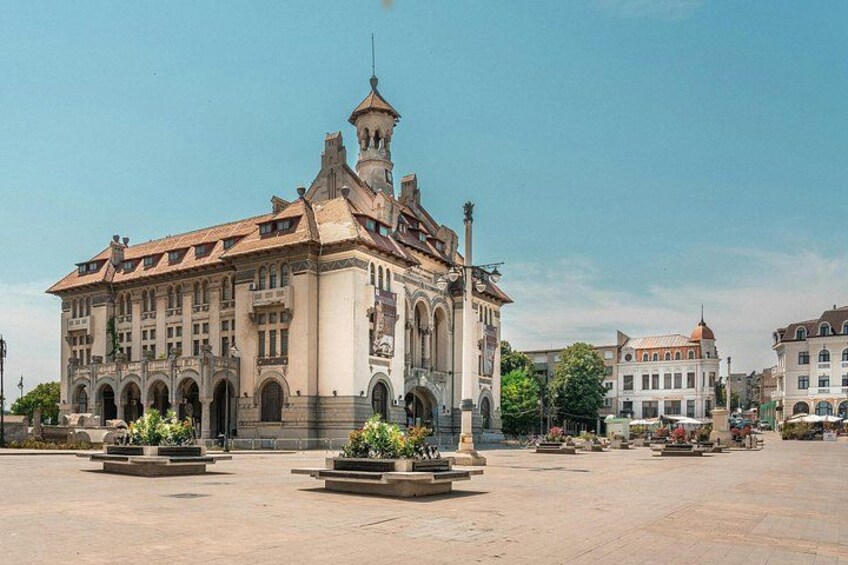 A historic building with arched windows and a tower, surrounded by a plaza with planters and benches. 2